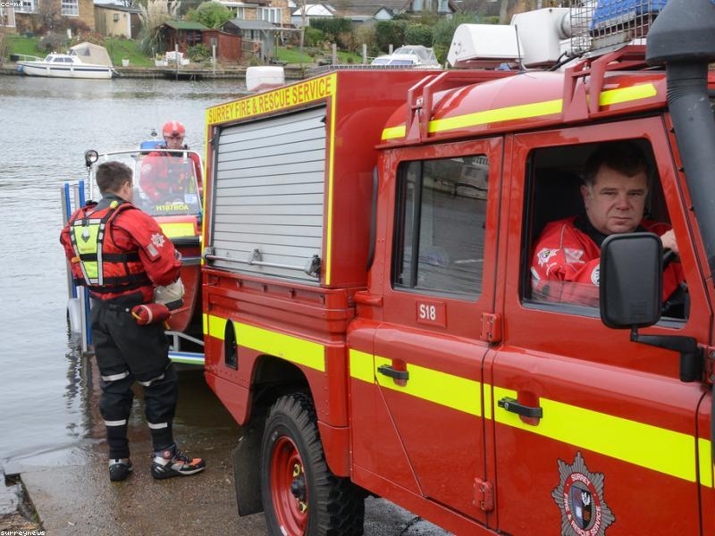 Fire and rescue crew beside a red emergency vehicle at the water's edge